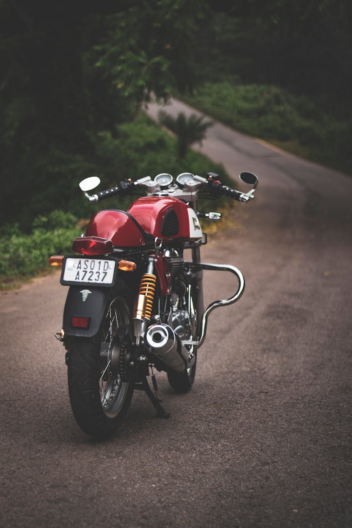 Rear view of a classic red motorcycle parked on a quiet country road, showcasing vintage style.